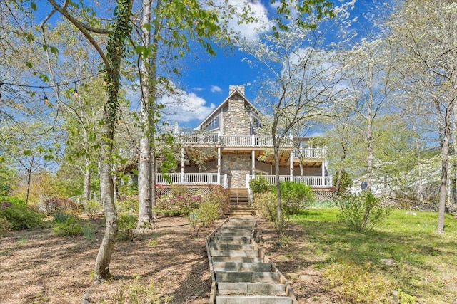 view of front of house with stone siding, a chimney, a balcony, and stairs