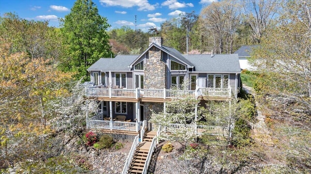 back of house featuring roof with shingles, stone siding, a chimney, and a deck