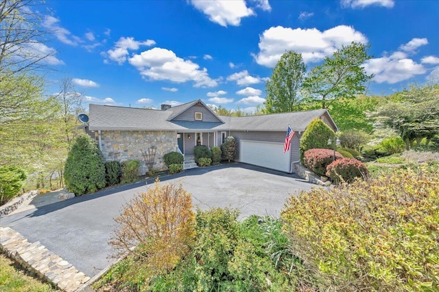 ranch-style home featuring a garage, stone siding, and aphalt driveway