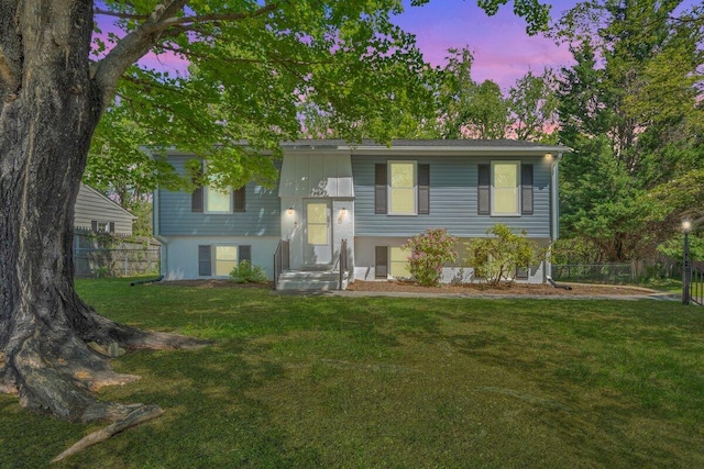 raised ranch featuring fence and a lawn