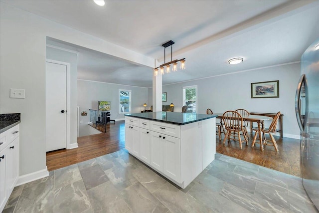 kitchen with white cabinets, a kitchen island, freestanding refrigerator, baseboards, and decorative light fixtures