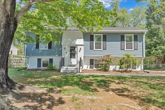split foyer home featuring brick siding, fence, board and batten siding, and a front yard