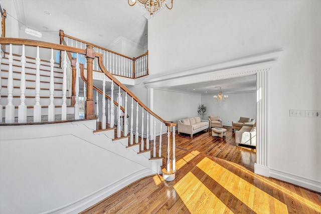 stairs with a chandelier, hardwood / wood-style floors, a towering ceiling, and ornamental molding