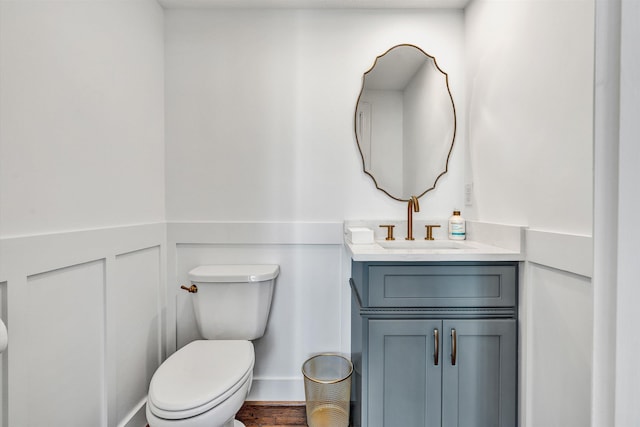 half bath featuring toilet, vanity, wood finished floors, and a wainscoted wall