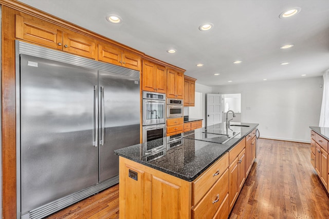 kitchen with hardwood / wood-style floors, stainless steel appliances, a kitchen island with sink, and a sink