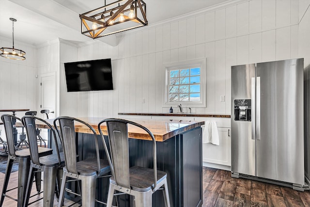 kitchen with white cabinets, dark wood finished floors, decorative light fixtures, stainless steel fridge, and a breakfast bar area