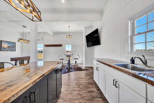 kitchen featuring white cabinets, a sink, beam ceiling, hanging light fixtures, and dark wood-style flooring