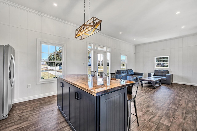 kitchen featuring stainless steel fridge with ice dispenser, a decorative wall, a breakfast bar, dark wood-type flooring, and ornamental molding