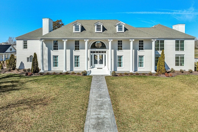 view of front of house featuring a chimney, a front lawn, and roof with shingles