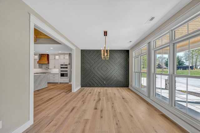 unfurnished dining area featuring a notable chandelier, light wood-style flooring, visible vents, and plenty of natural light