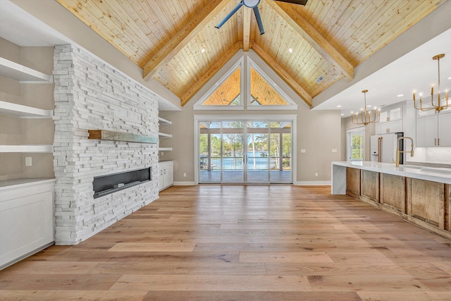unfurnished living room featuring light wood finished floors, beam ceiling, ceiling fan with notable chandelier, wood ceiling, and a stone fireplace