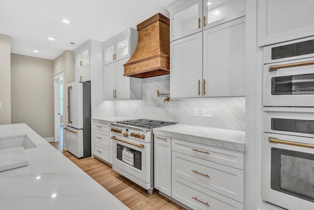 kitchen featuring custom exhaust hood, light stone counters, white appliances, white cabinetry, and recessed lighting