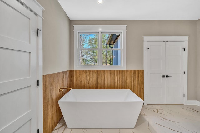 full bath with recessed lighting, marble finish floor, wooden walls, wainscoting, and a soaking tub