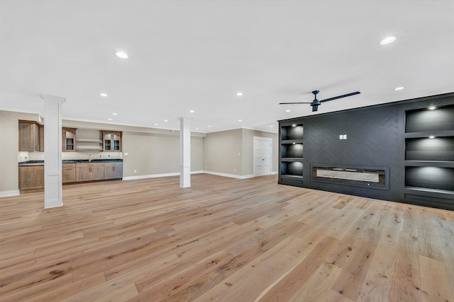unfurnished living room with ornate columns, baseboards, and light wood-style flooring
