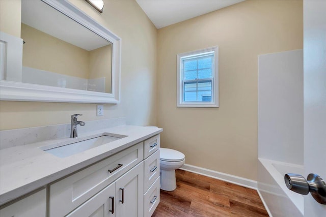 full bathroom with wood finished floors, toilet, vanity, baseboards, and a tub