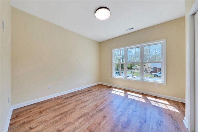 empty room with wood finished floors, visible vents, and baseboards