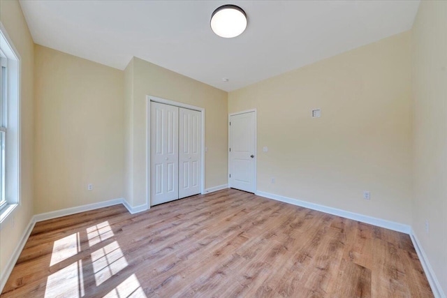 unfurnished bedroom with light wood-type flooring, a closet, and baseboards