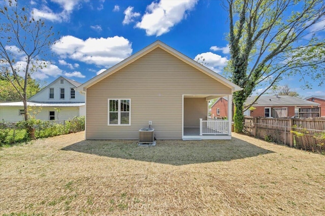 rear view of house featuring central air condition unit, a lawn, and fence