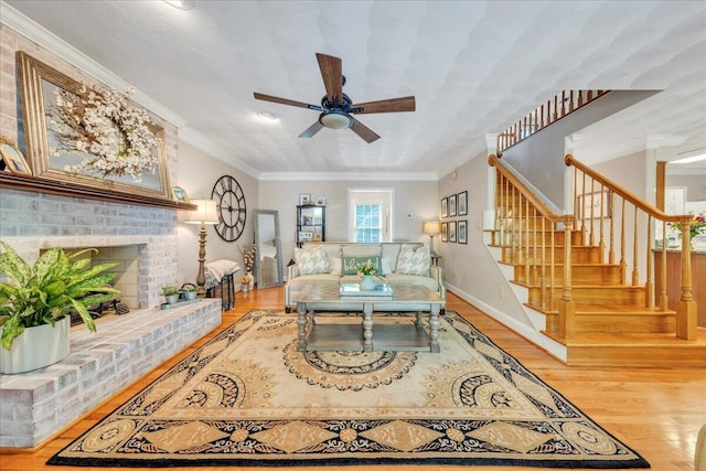 living room with ceiling fan, crown molding, a brick fireplace, stairway, and light wood-style floors