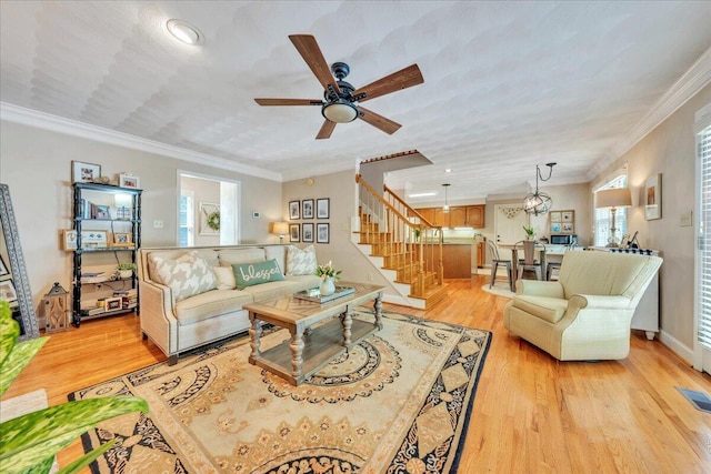 living area featuring crown molding, a healthy amount of sunlight, stairway, light wood-type flooring, and a ceiling fan