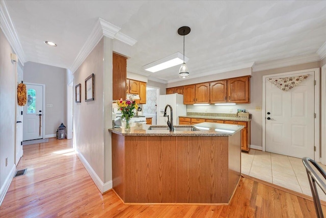 kitchen featuring brown cabinets, a sink, a peninsula, light wood-type flooring, and ornamental molding
