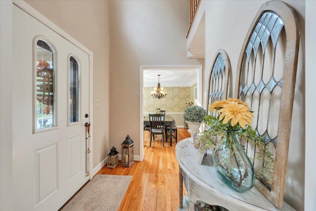 entryway featuring baseboards, a high ceiling, wood finished floors, and a chandelier