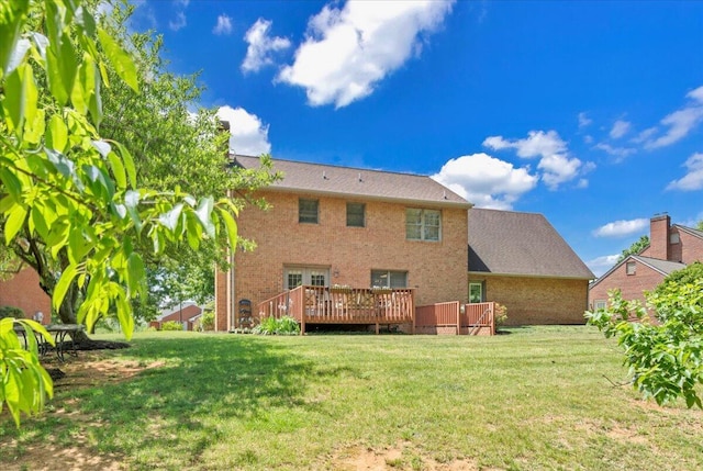 rear view of property featuring brick siding, a wooden deck, and a yard