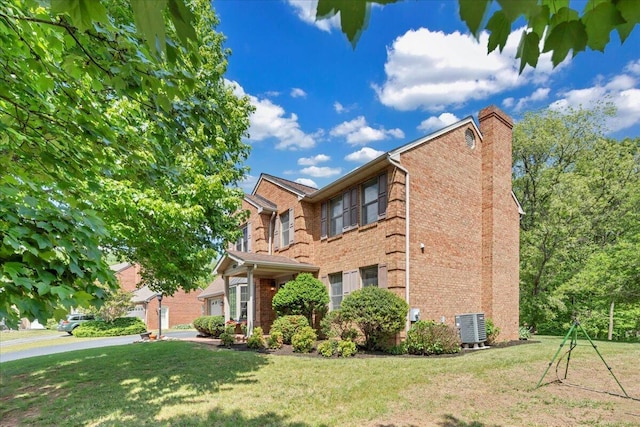 view of side of property with a yard, brick siding, a chimney, and central AC unit