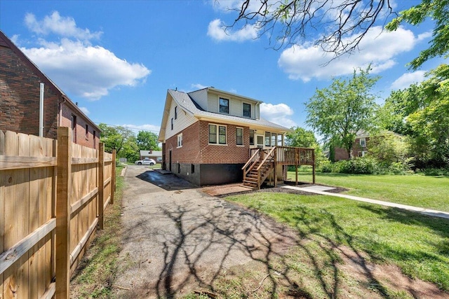 rear view of house featuring stairway, brick siding, a wooden deck, and a lawn