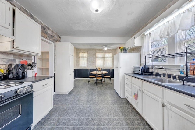 kitchen with range with gas stovetop, dark countertops, white cabinets, ceiling fan, and a textured ceiling