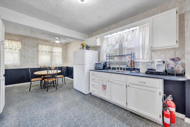 kitchen with freestanding refrigerator, a sink, white cabinets, a ceiling fan, and baseboards