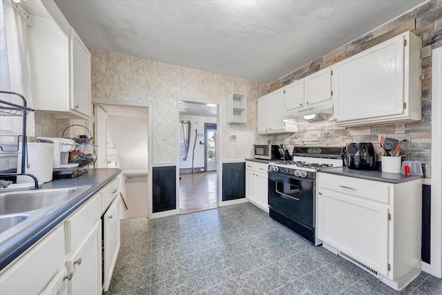 kitchen with range with gas stovetop, under cabinet range hood, stainless steel microwave, white cabinetry, and dark countertops