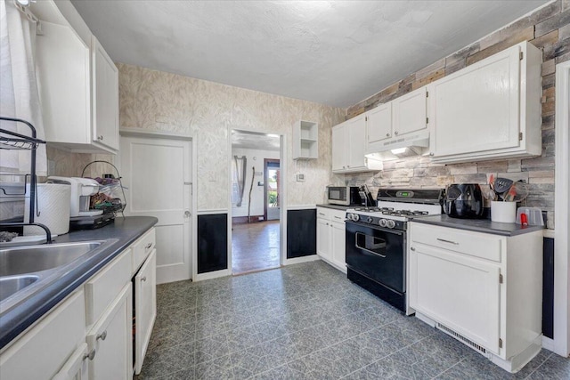 kitchen featuring gas range, under cabinet range hood, stainless steel microwave, dark countertops, and white cabinets