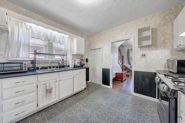 kitchen featuring gas range, a sink, dark countertops, white cabinets, and wallpapered walls