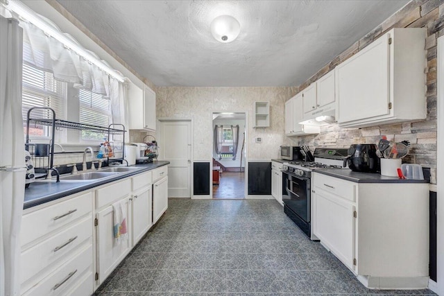 kitchen with black range with gas stovetop, dark countertops, dark flooring, and white cabinetry