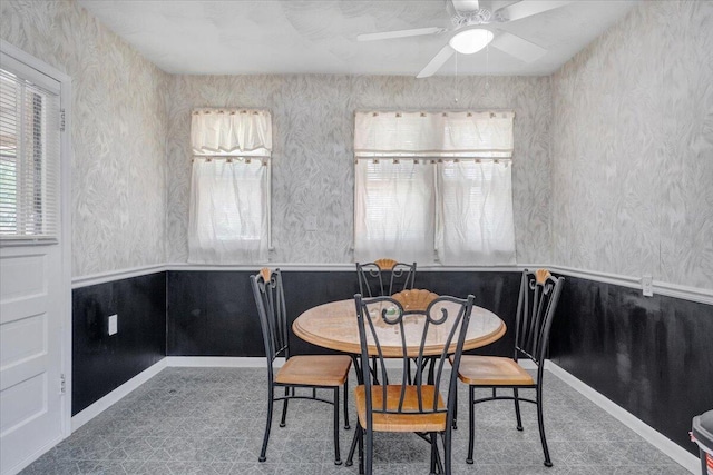 dining area with healthy amount of natural light, ceiling fan, wallpapered walls, and a wainscoted wall
