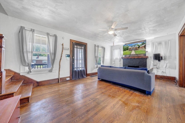 living area featuring a stone fireplace, wood finished floors, ceiling fan, healthy amount of natural light, and a textured ceiling