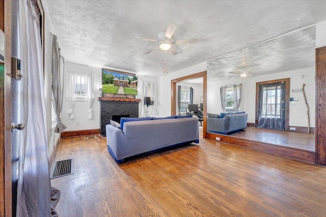 living area featuring ceiling fan, wood finished floors, plenty of natural light, a brick fireplace, and a textured ceiling