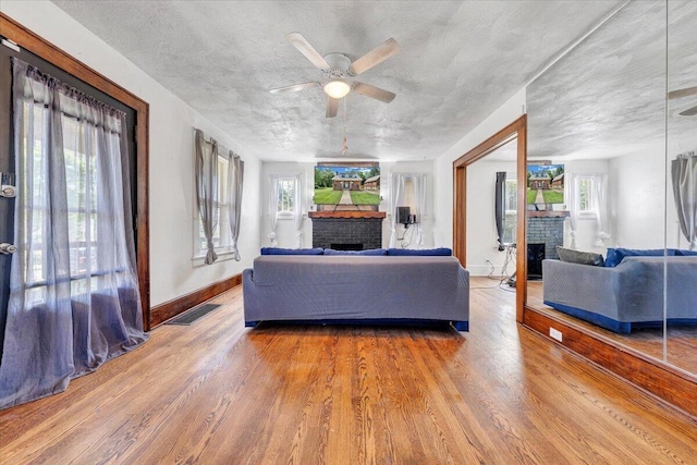 living room featuring a brick fireplace, ceiling fan, wood finished floors, baseboards, and a textured ceiling
