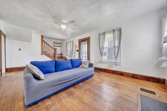 living area with baseboards, stairs, wood finished floors, a ceiling fan, and a textured ceiling