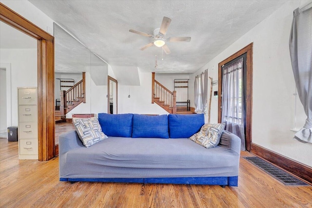 living area with stairs, wood finished floors, ceiling fan, and a textured ceiling