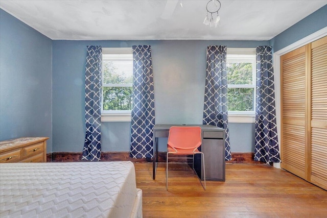 bedroom with multiple windows, wood finished floors, a closet, and baseboards