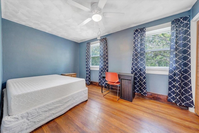 bedroom featuring multiple windows, wood finished floors, a ceiling fan, and baseboards