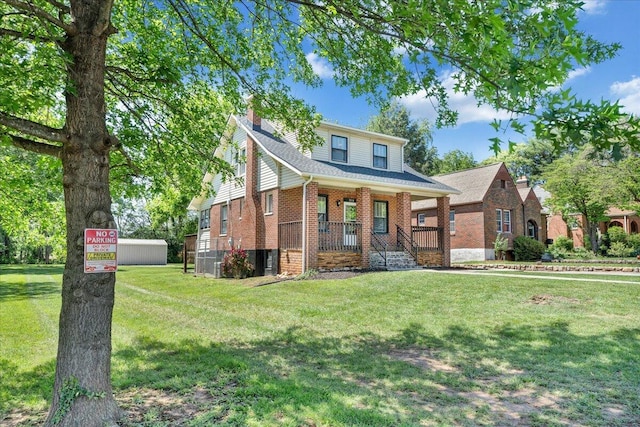 view of front of home featuring a chimney, covered porch, brick siding, a front lawn, and a shingled roof
