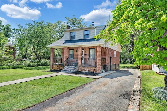 view of front facade with covered porch, a chimney, driveway, a front lawn, and brick siding