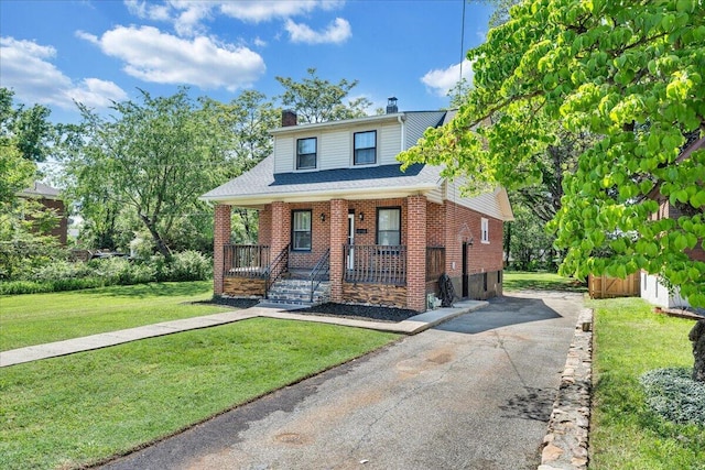 view of front of house with covered porch, a chimney, driveway, a front lawn, and brick siding