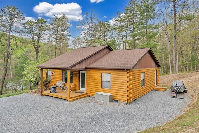 rear view of house featuring a wooded view, driveway, a deck, log siding, and roof with shingles