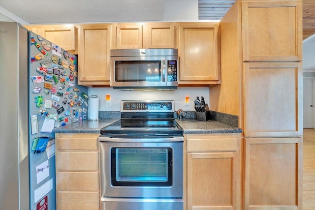 kitchen featuring stainless steel appliances, light brown cabinetry, and dark countertops