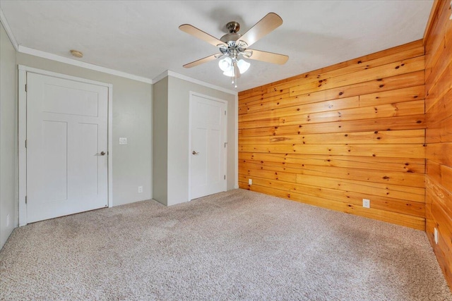 unfurnished bedroom featuring a ceiling fan, crown molding, a closet, wooden walls, and carpet floors
