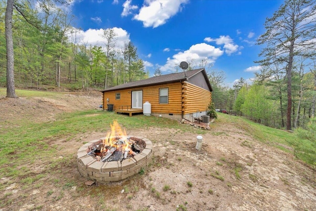 rear view of house featuring a fire pit, a forest view, log exterior, and crawl space